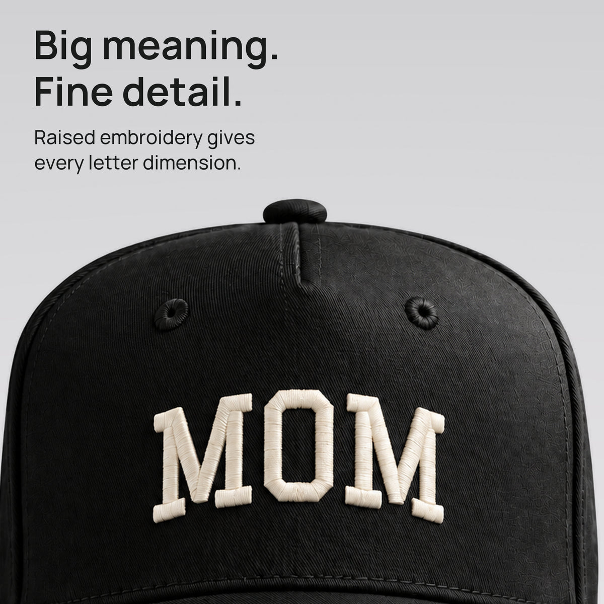 Close-up of ivory MOM embroidery on the black cap. Fine detail. Raised collegiate lettering on cotton twill.