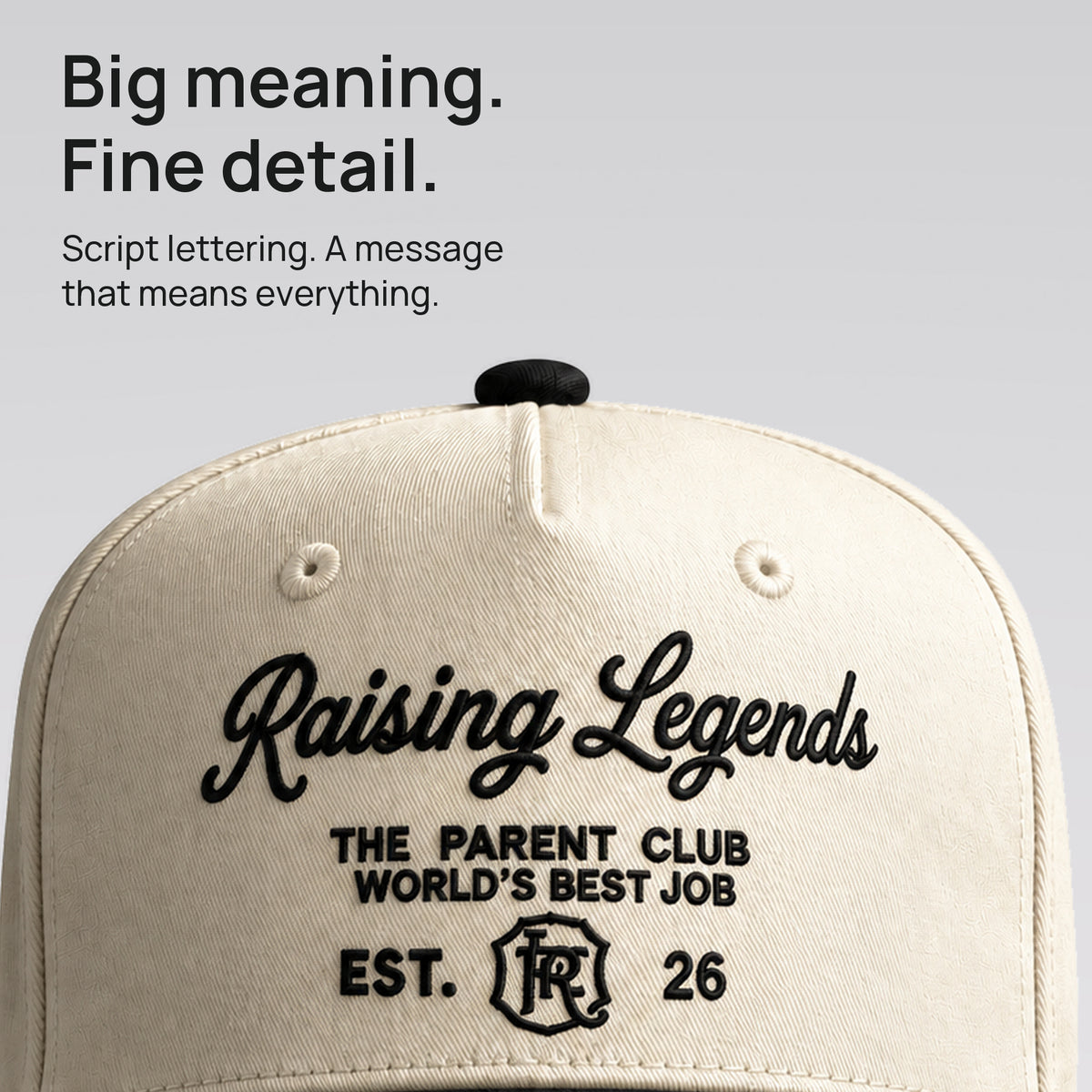 Close detail of black Raising Legends script embroidered on cream cotton twill. Big meaning. Fine detail.