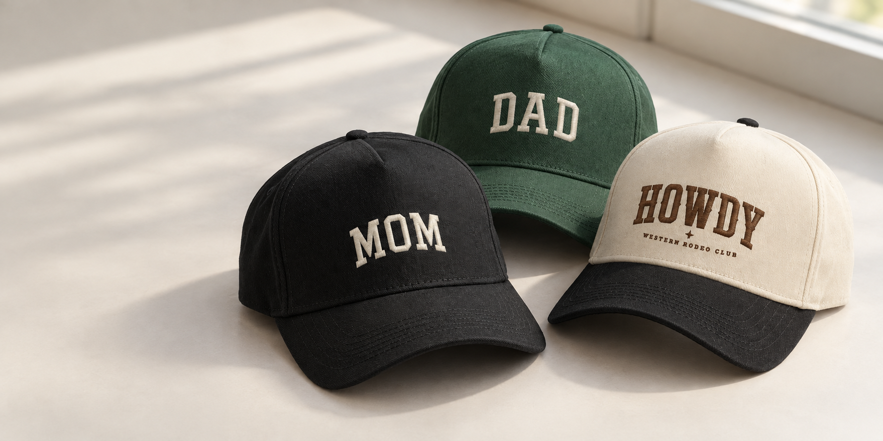 MOM, DAD, and HOWDY hats resting on an off-white table in natural window light
